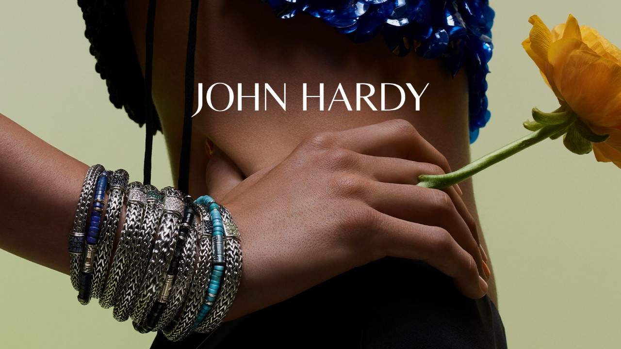 A model with the different collections of John Hardy Bracelets. Holding a yellow flower which is native to Bali.